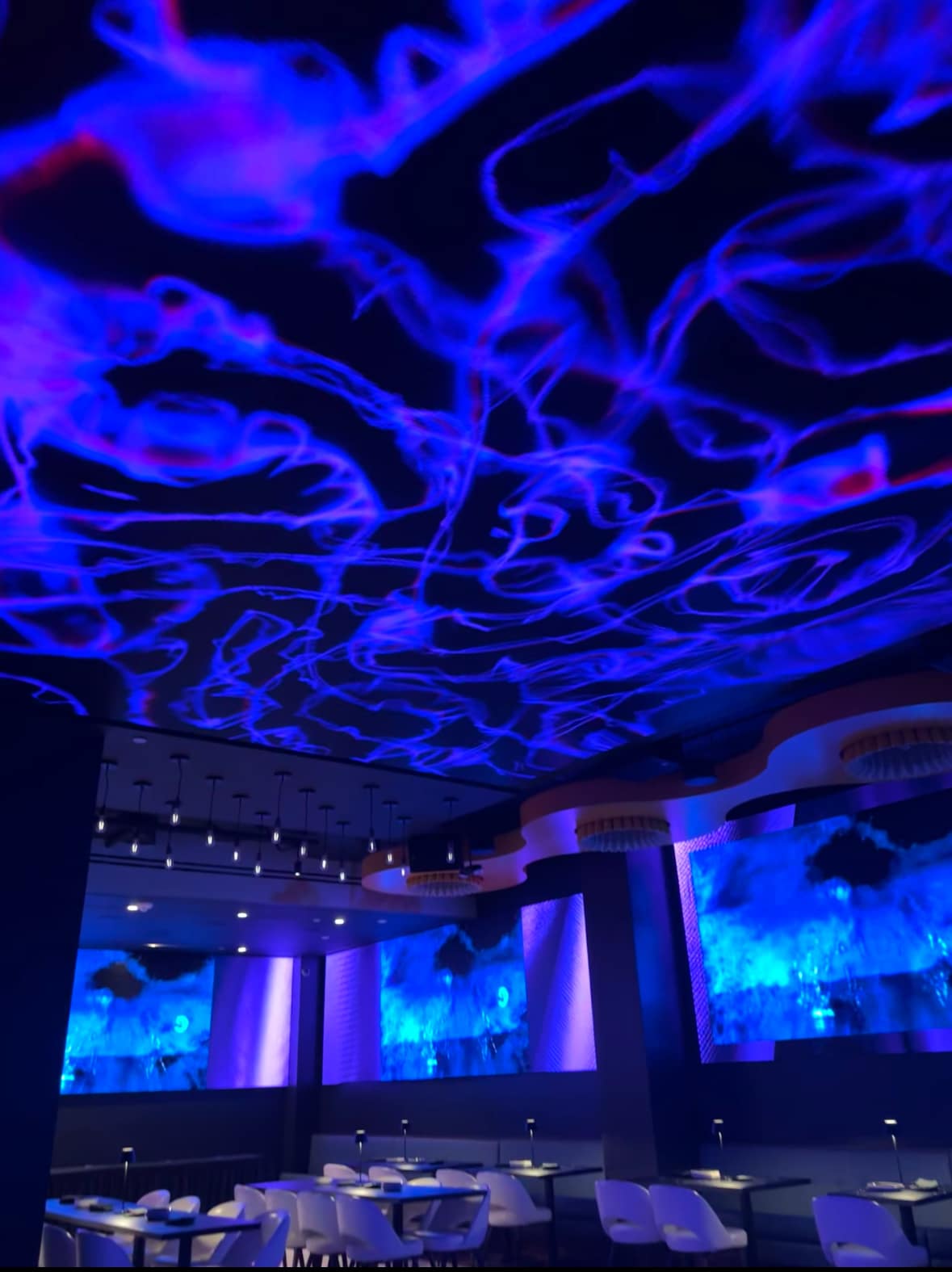 Interior of Planet Hollywood NYC with futuristic blue lighting, abstract ceiling patterns, and modern dining tables.